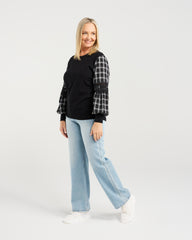 Woman wearing a black sweater with plaid sleeves and light blue jeans on a white background