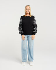 Woman wearing a black sweater with plaid sleeves and light blue jeans on a white background