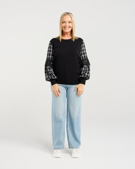 Woman wearing a black sweater with plaid sleeves and light blue jeans on a white background