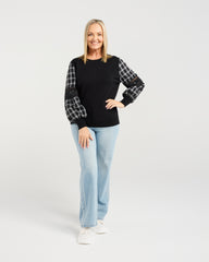 Woman wearing a black sweater with plaid sleeves and light blue jeans on a white background