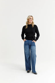 Woman wearing a black sweater and blue jeans on a white background