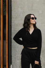 Woman wearing a black outfit with sunglasses against a gray wall.