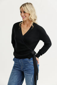 Woman wearing a black wrap sweater and blue jeans on a white background
