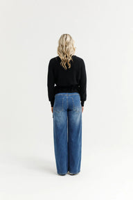 Person wearing a black sweater and blue jeans on a white background