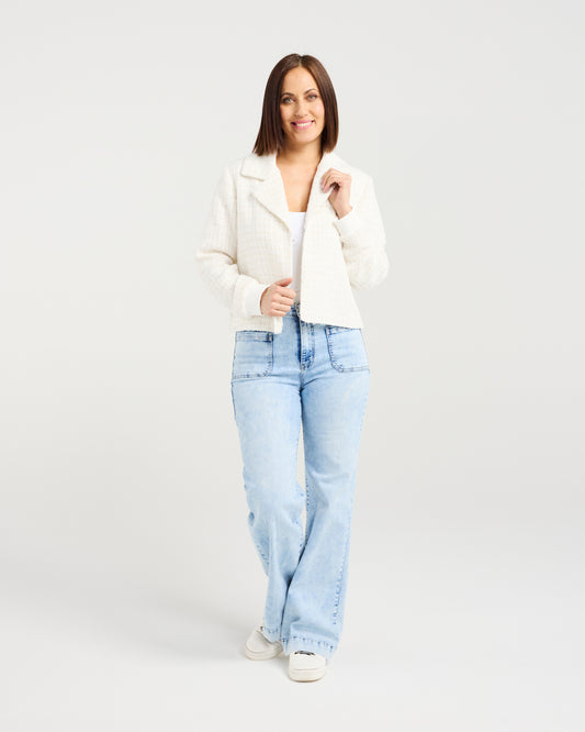 Woman wearing a white jacket and light blue jeans on a plain background