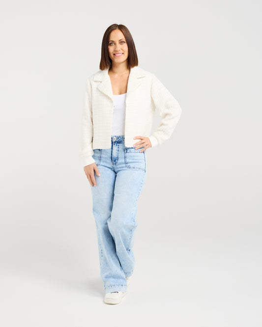 Woman wearing a white jacket and light blue jeans on a plain background