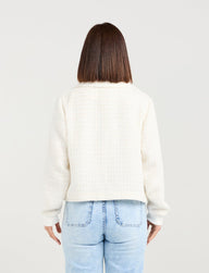 Person wearing a white sweater and light blue jeans on a plain background