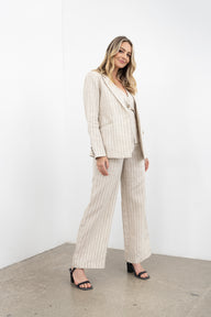 Woman wearing a beige pinstripe suit standing against a white wall.
