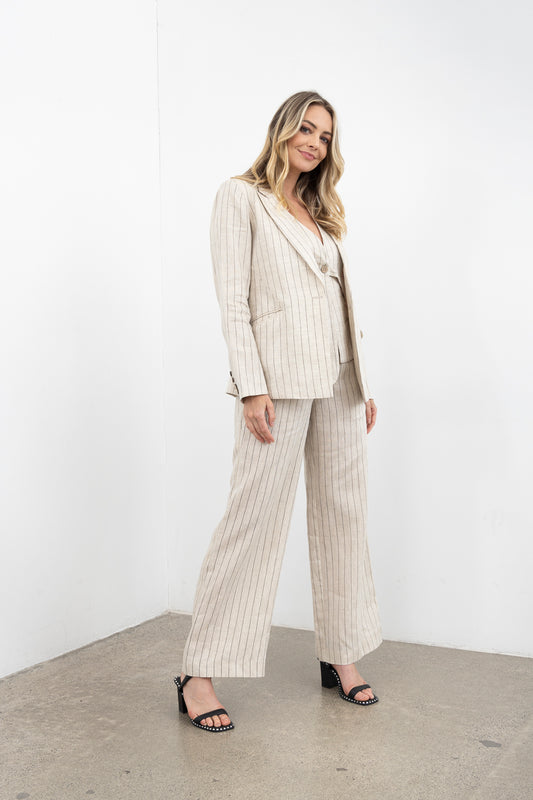 Woman wearing a beige pinstripe suit standing against a white wall.
