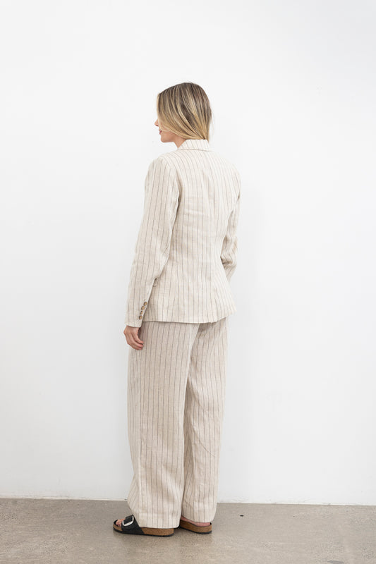 Person wearing a beige pinstripe suit standing against a white wall.