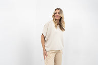 Woman wearing a white sweater and beige pants against a white background