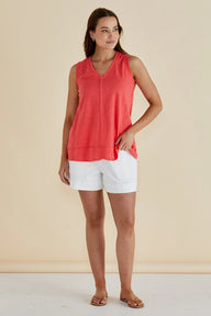Woman wearing a coral sleeveless top and white shorts against a beige background