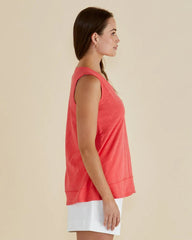 Woman wearing a coral sleeveless top and white shorts on a beige background