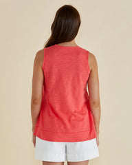 Woman wearing a coral sleeveless top and white shorts on a beige background