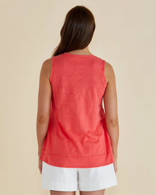 Woman wearing a coral sleeveless top and white shorts on a beige background