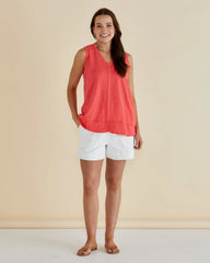 Woman wearing a coral sleeveless top and white shorts against a beige background