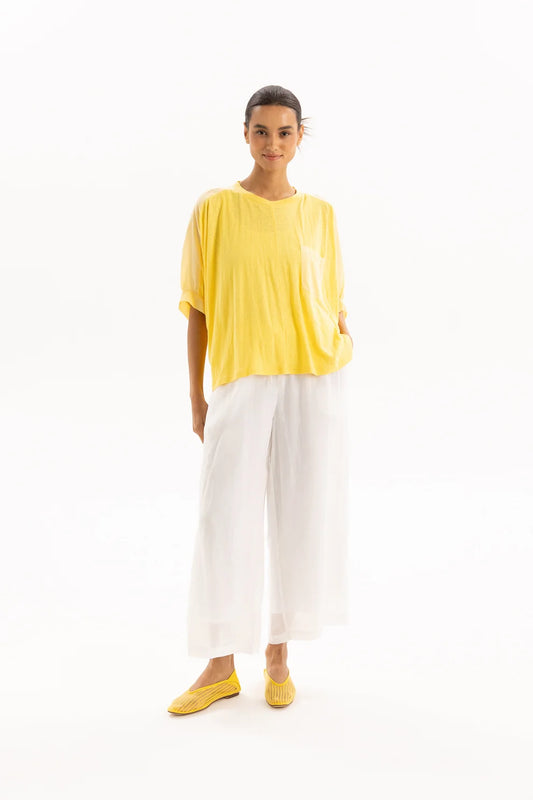 A woman modeling a bright yellow short-sleeve top and white wide-leg pants against a clean white studio background.