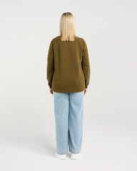 Person wearing an olive green sweatshirt and light blue jeans on a white background