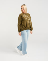 Woman wearing an olive green hoodie with a graphic design and light blue jeans on a white background