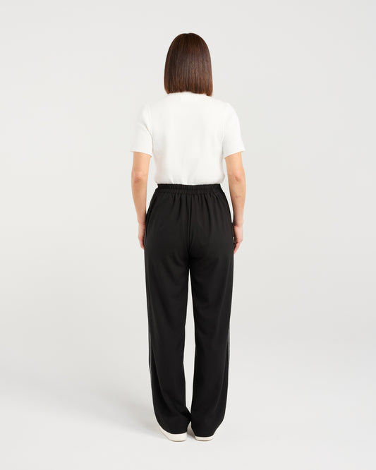 Person wearing black wide-leg pants and a white top on a light gray background