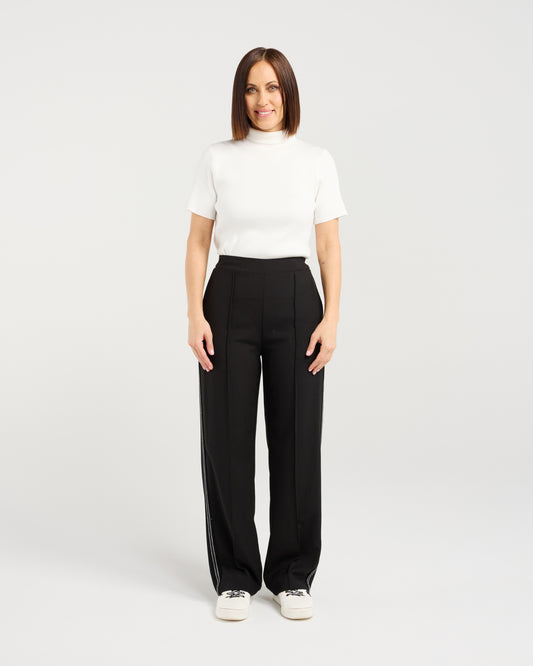 Woman wearing a white top and black pants on a plain background