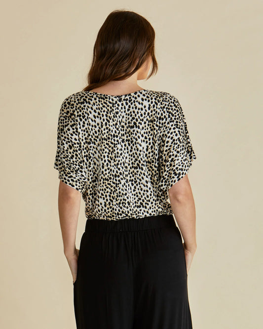 Woman wearing a leopard print top and black pants on a beige background