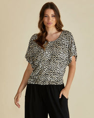 Woman wearing a leopard print top and black pants on a beige background