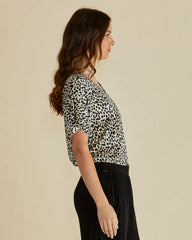 Woman wearing a leopard print top and black pants against a beige background