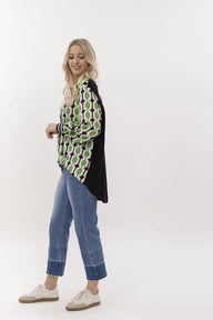 Woman wearing a patterned shirt, black cardigan, and blue jeans on a white background