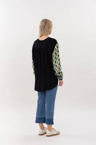 Person wearing a black top with green and white patterned sleeves and blue jeans on a white background