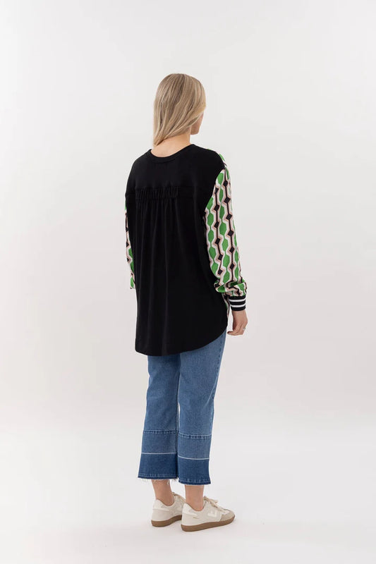 Person wearing a black top with green and white patterned sleeves and blue jeans on a white background