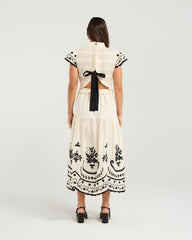 Woman wearing a white dress with black embroidery and a bow at the back on a light gray background
