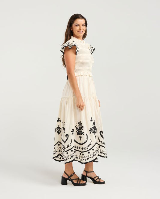 Woman wearing a white dress with black embroidery on a light gray background