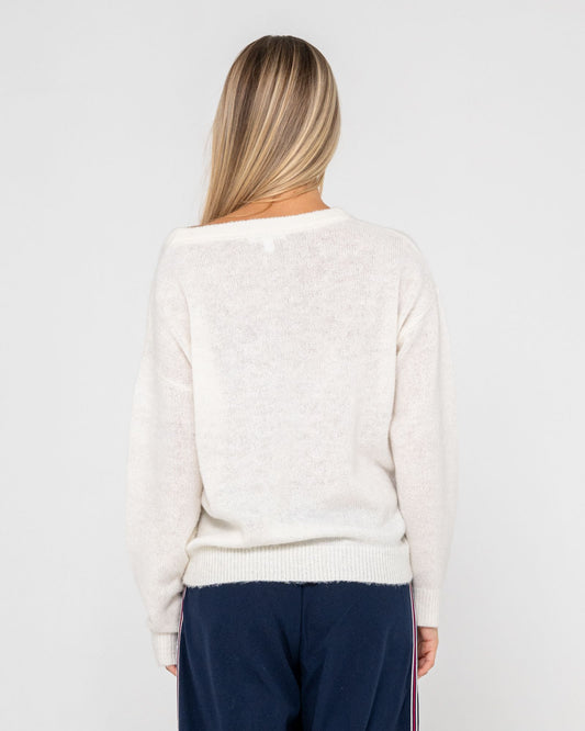 Person wearing a white sweater and navy pants on a plain background