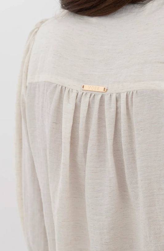 Close-up of a beige blouse with a brand label on a white background