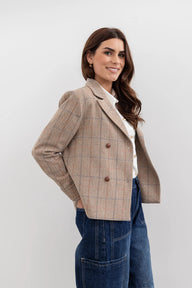 Woman wearing a beige checkered blazer over a white shirt with blue jeans on a light gray background