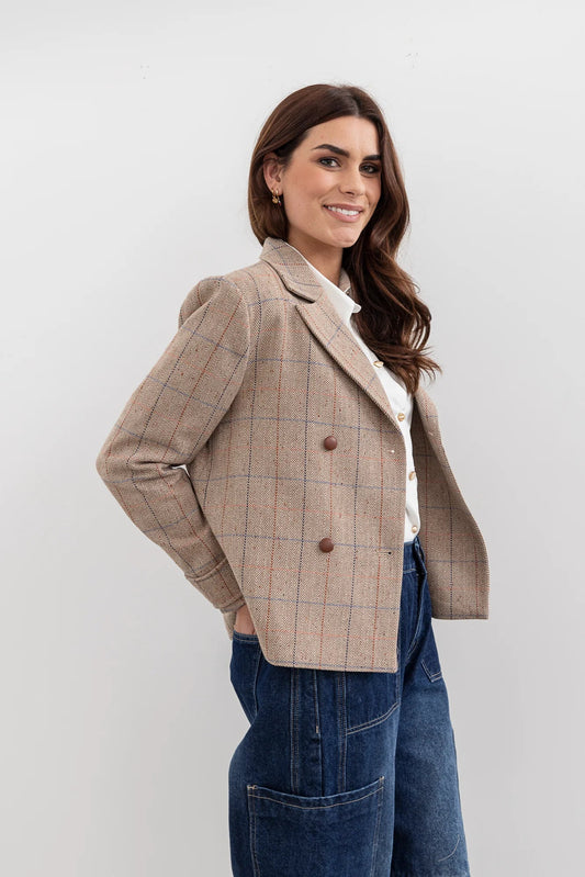 Woman wearing a beige checkered blazer over a white shirt with blue jeans on a light gray background