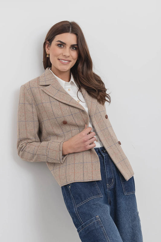 Woman wearing a beige checkered jacket and blue jeans against a white background