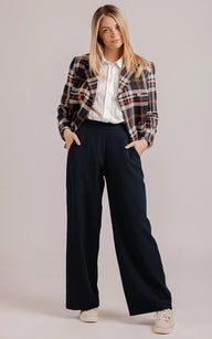 Woman wearing a plaid jacket, white shirt, and dark pants on a plain background