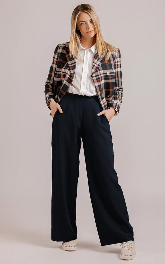 Woman wearing a plaid jacket, white shirt, and dark pants on a plain background
