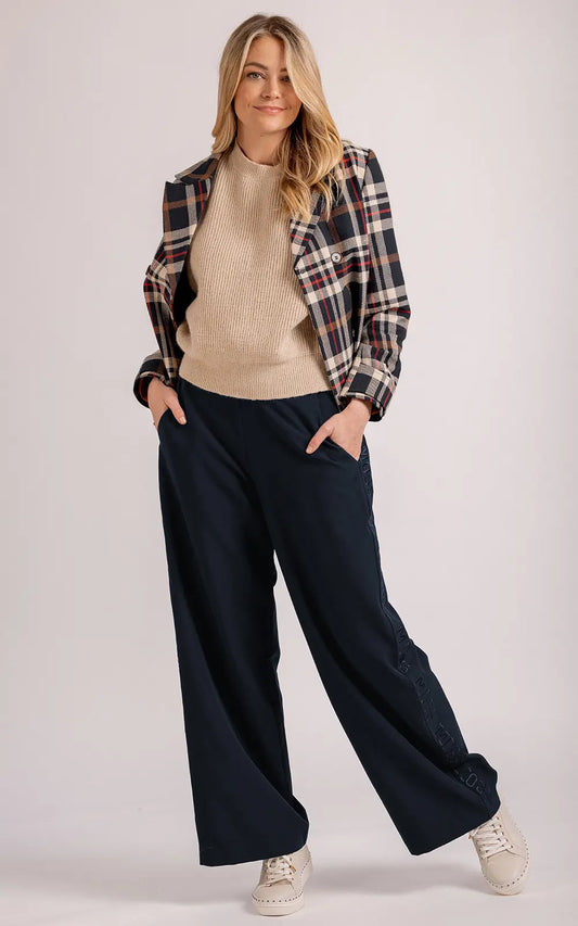 Woman wearing a plaid blazer, beige sweater, and navy wide-leg pants on a plain background
