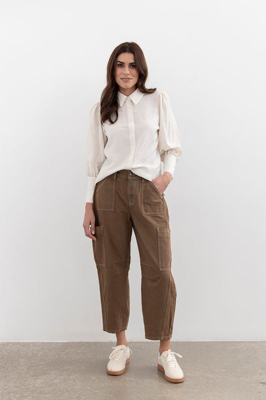 Woman wearing a white blouse and brown pants against a plain background