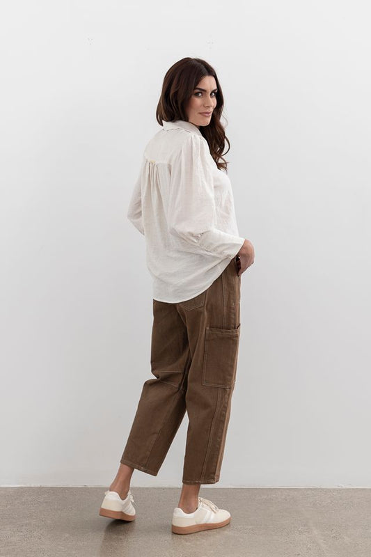 Woman wearing a white shirt and brown pants against a plain background