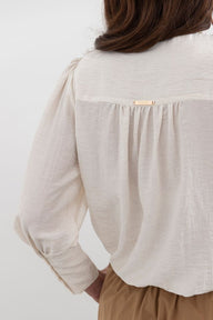 Close-up of a person wearing a light beige blouse with a white background