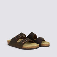 A pair of dark brown double-strap slide sandals with adjustable metal buckles, cork-look soles, and tan footbeds, photographed on a light gray background.