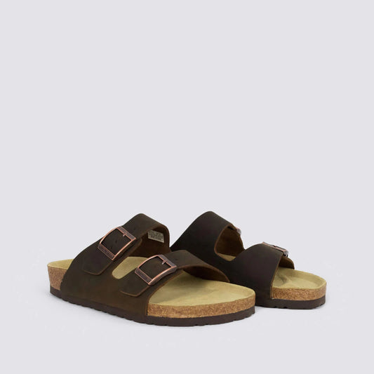 A pair of dark brown double-strap slide sandals with adjustable metal buckles, cork-look soles, and tan footbeds, photographed on a light gray background.