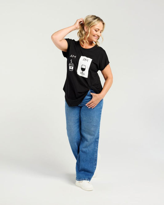A woman modeling a black short-sleeve graphic t-shirt with white text and illustrations, paired with blue jeans and white sneakers, against a light gray studio background.