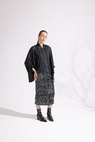 Person wearing a black outfit with a patterned skirt on a white background