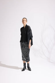 Person wearing a black jacket, patterned skirt, and black boots on a white background