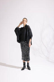 Person wearing a black outfit with a patterned skirt on a white background